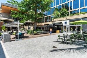 An outdoor patio area with seating, a large tree, and a building with a restaurant in the background. - Breathtaking Direct Bay Views: 2/2.5 Condo includes Parking (Miami)