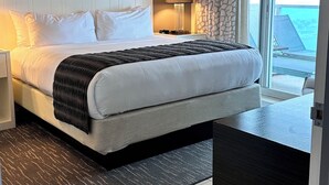 A modern hotel room with a large bed, a desk, and a view of the ocean.