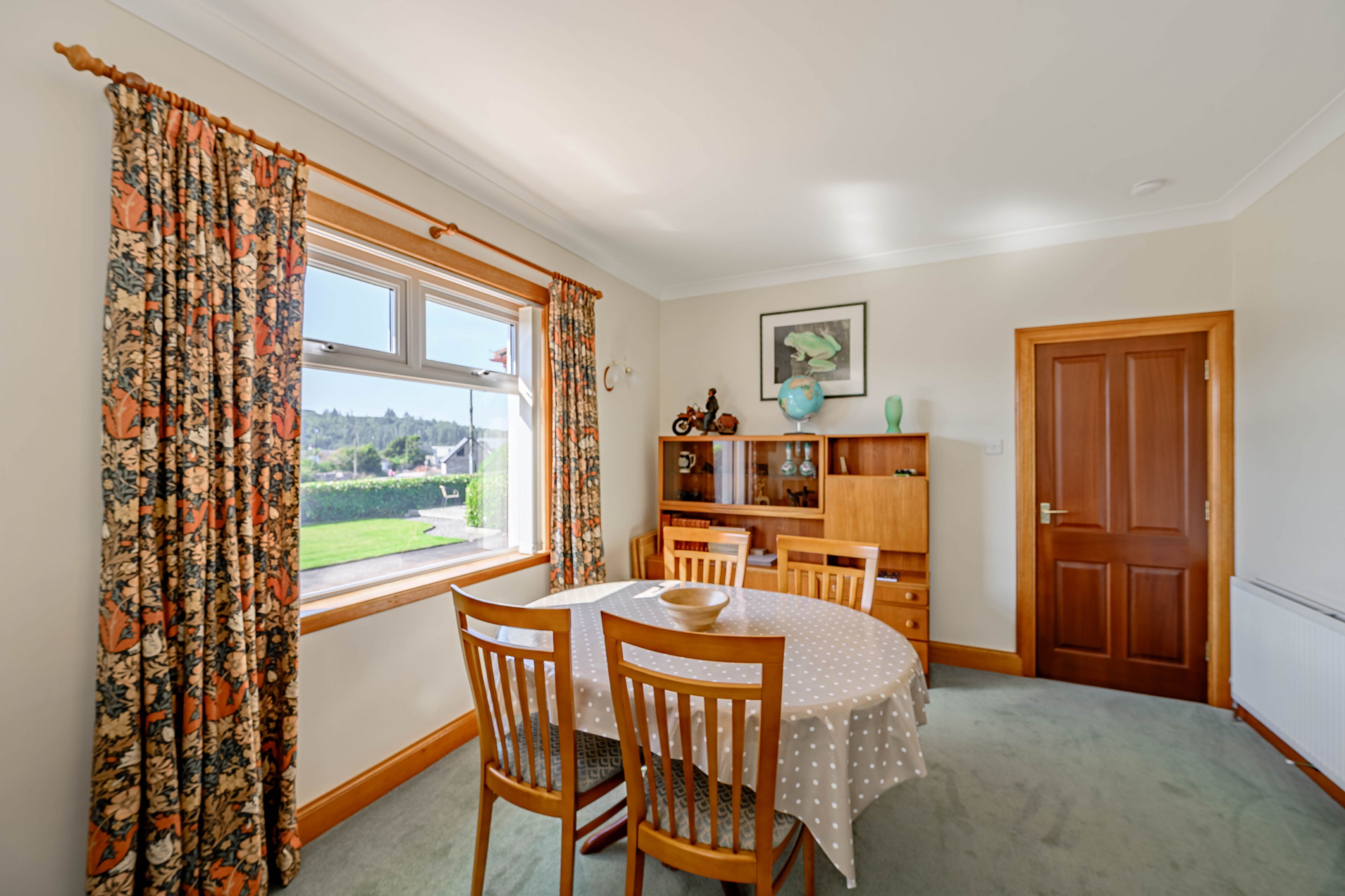 A dining area with a round table, wooden chairs, and a view of a garden through a window.