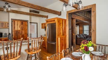 Un coin repas rustique avec des chaises en bois, une table en bois dressée pour deux personnes et un réfrigérateur en arrière-plan.