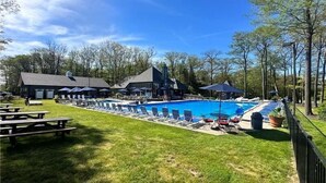 Ein Swimmingpool mit Liegestühlen, Picknicktischen und einem Gebäude mit Satteldach.