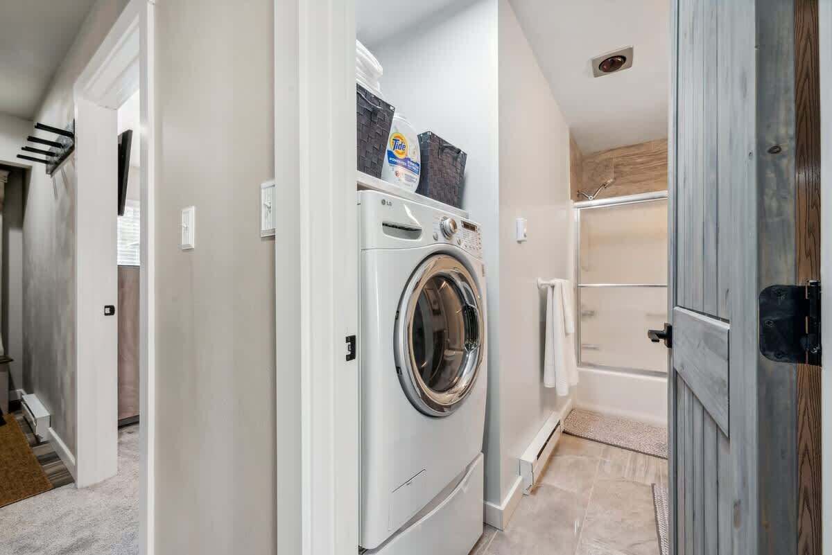 Une buanderie équipée d’un lave-linge à chargement frontal, d’un étendoir et d’un espace douche.