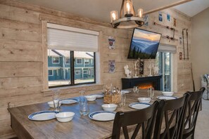 Un coin repas avec une table en bois dressée pour quatre personnes, une cheminée et un téléviseur fixé au mur.