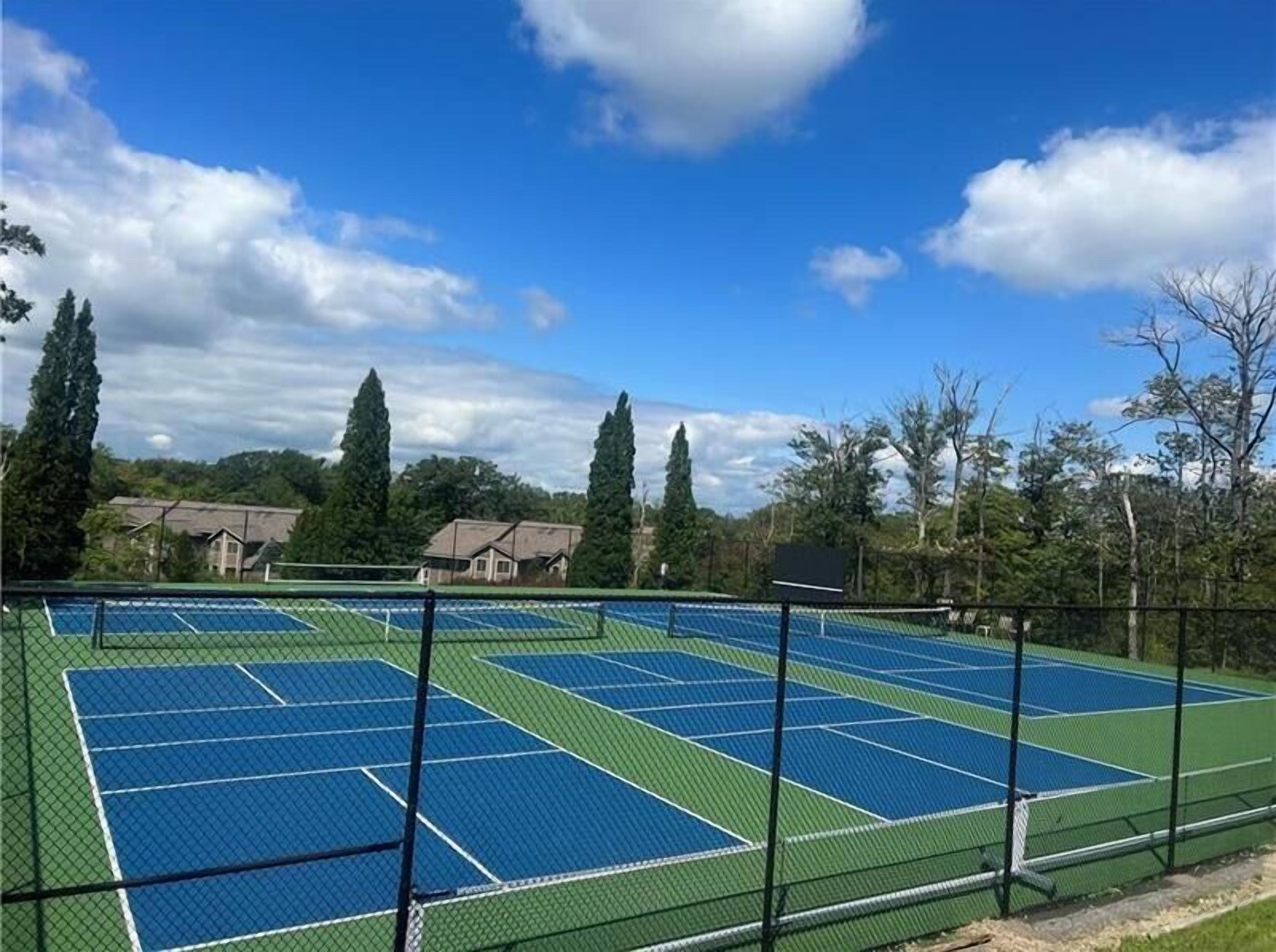 A tennis court with multiple courts, surrounded by trees and buildings.