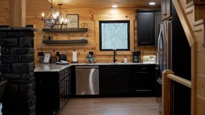 A kitchen with wooden walls, a stone accent wall, a chandelier, a coffee maker, and a refrigerator.