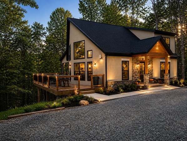 A modern two-story house with a deck, stone accents, and a gravel driveway.