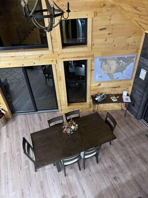 A wooden cabin interior with a dining table, chairs, a chandelier, a TV, and a map on the wall. - The Quana -  Hot tub|Huge Entertainment Room (Logan)