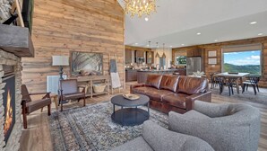 A spacious living area with a fireplace, leather sofa, and a dining table with chairs. - Hang Yer Hat - Breathtaking Views + Elegant Modern Interiors! (Sevierville)