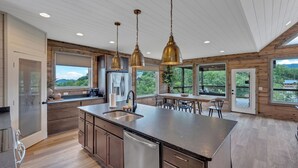 A modern kitchen with a large island, stainless steel appliances, and pendant lighting. - Hang Yer Hat - Breathtaking Views + Elegant Modern Interiors! (Sevierville)