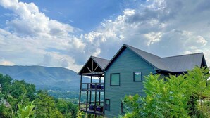 A house with a balcony, surrounded by lush greenery and mountains in the background. - Hang Yer Hat - Breathtaking Views + Elegant Modern Interiors! (Sevierville)