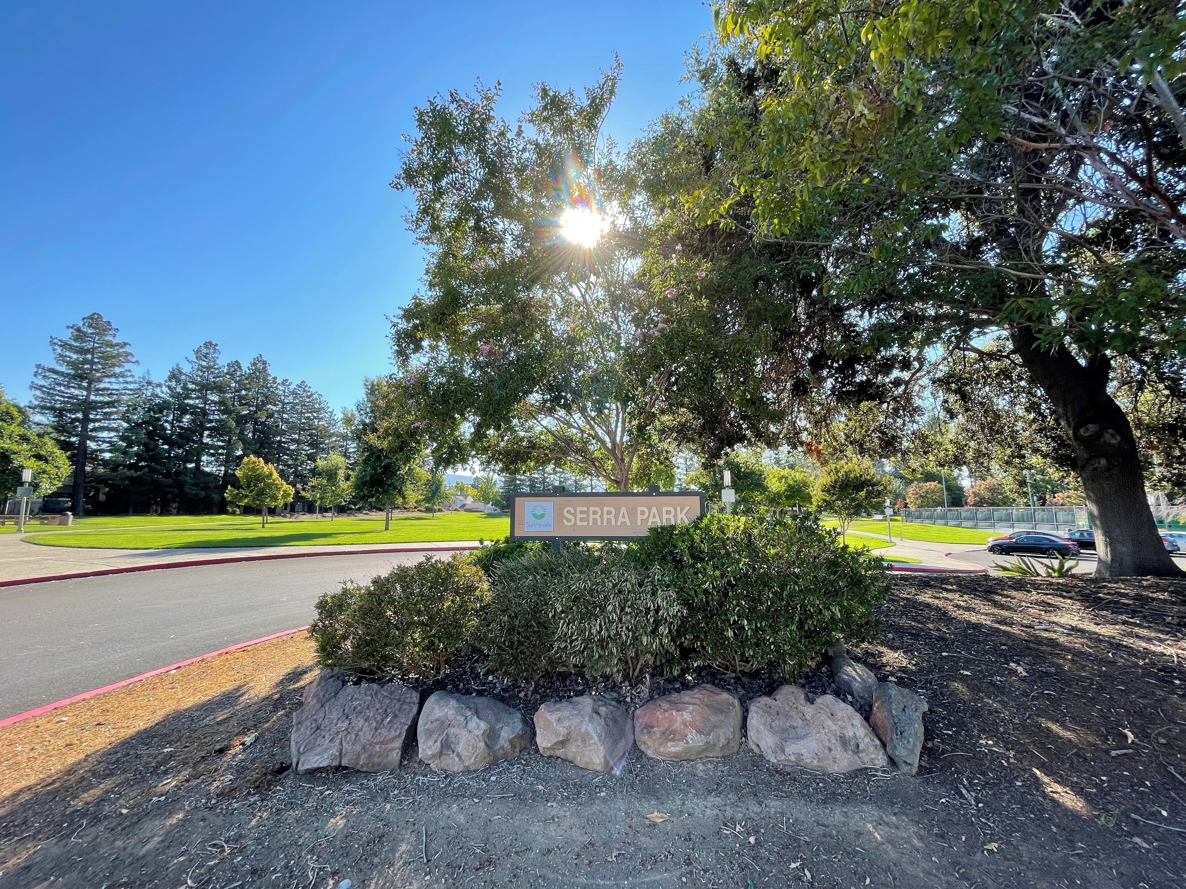 A sign for Serra Park with a clear sky and trees in the background.