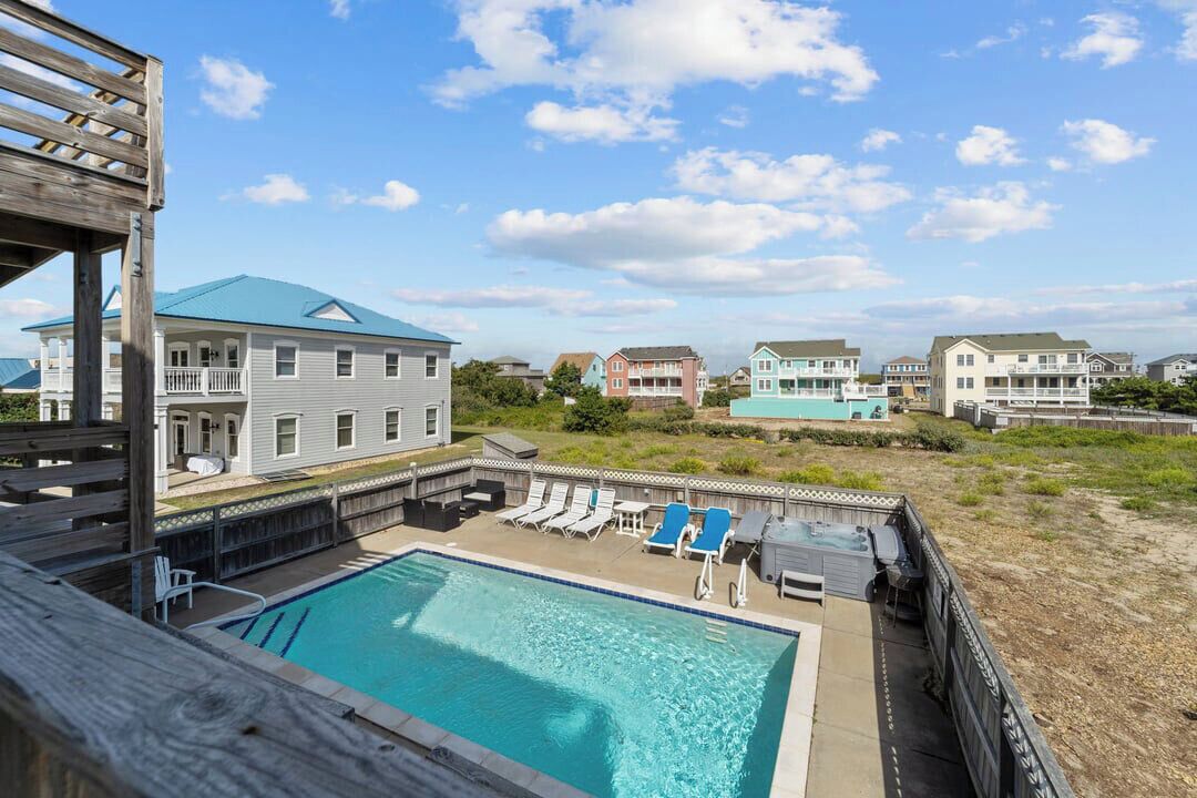 A swimming pool with lounge chairs, a wooden deck, and a view of surrounding buildings.