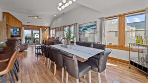 A spacious dining area with a long table and multiple chairs, a bar area with stools, and a view of the outside through large windows.
