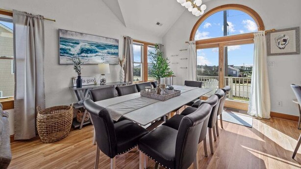 A dining area with a large table, black chairs, and a view of the outdoors through a large arched window.