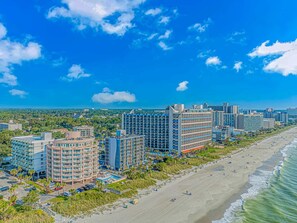 A coastal hotel with multiple high-rise buildings, a beach, and a clear blue sky. - St Clements 704 (Myrtle Beach)