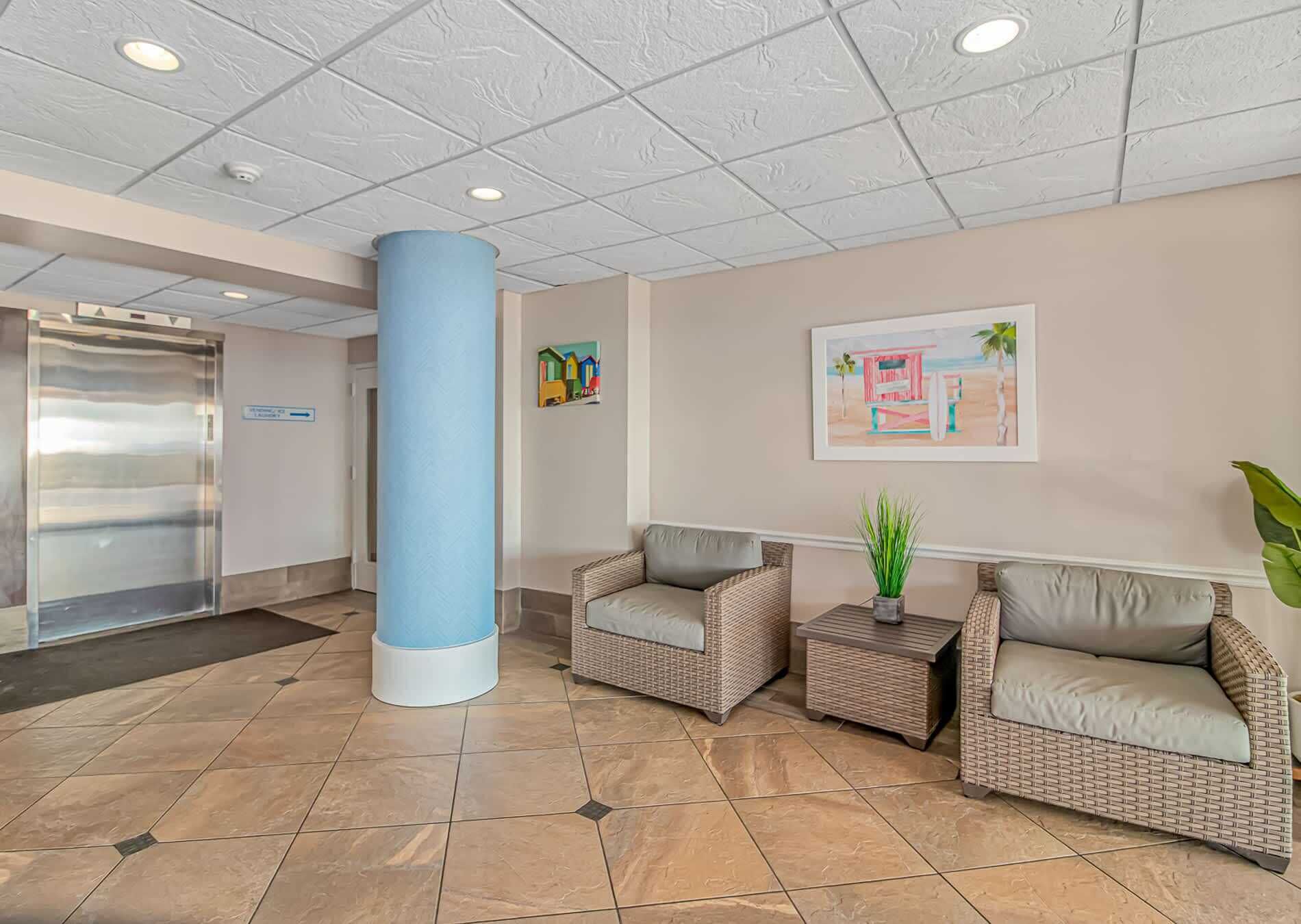 A lobby with a reception desk, a large blue pillar, wicker chairs, and a framed picture on the wall.
