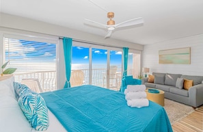 A bedroom with a bed, a sofa, a ceiling fan, and a view of the ocean.