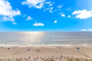 A beach with a clear sky, calm sea, and people enjoying the sand.