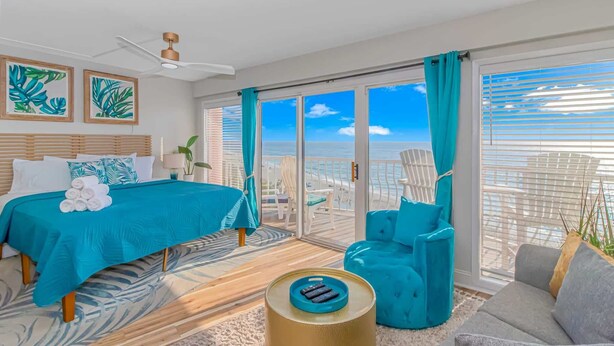 A room with a bed, a sofa, a chair, a small table, a ceiling fan, and a view of the ocean through large glass doors. - St Clements 704 (Myrtle Beach)