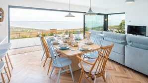 A modern dining area with a view of the sea, a sofa, and a TV.