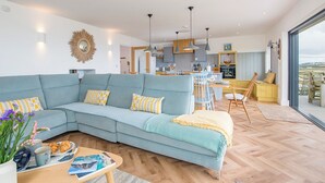 A modern living room with a light blue sofa, a dining area with wooden chairs, and a kitchen in the background.