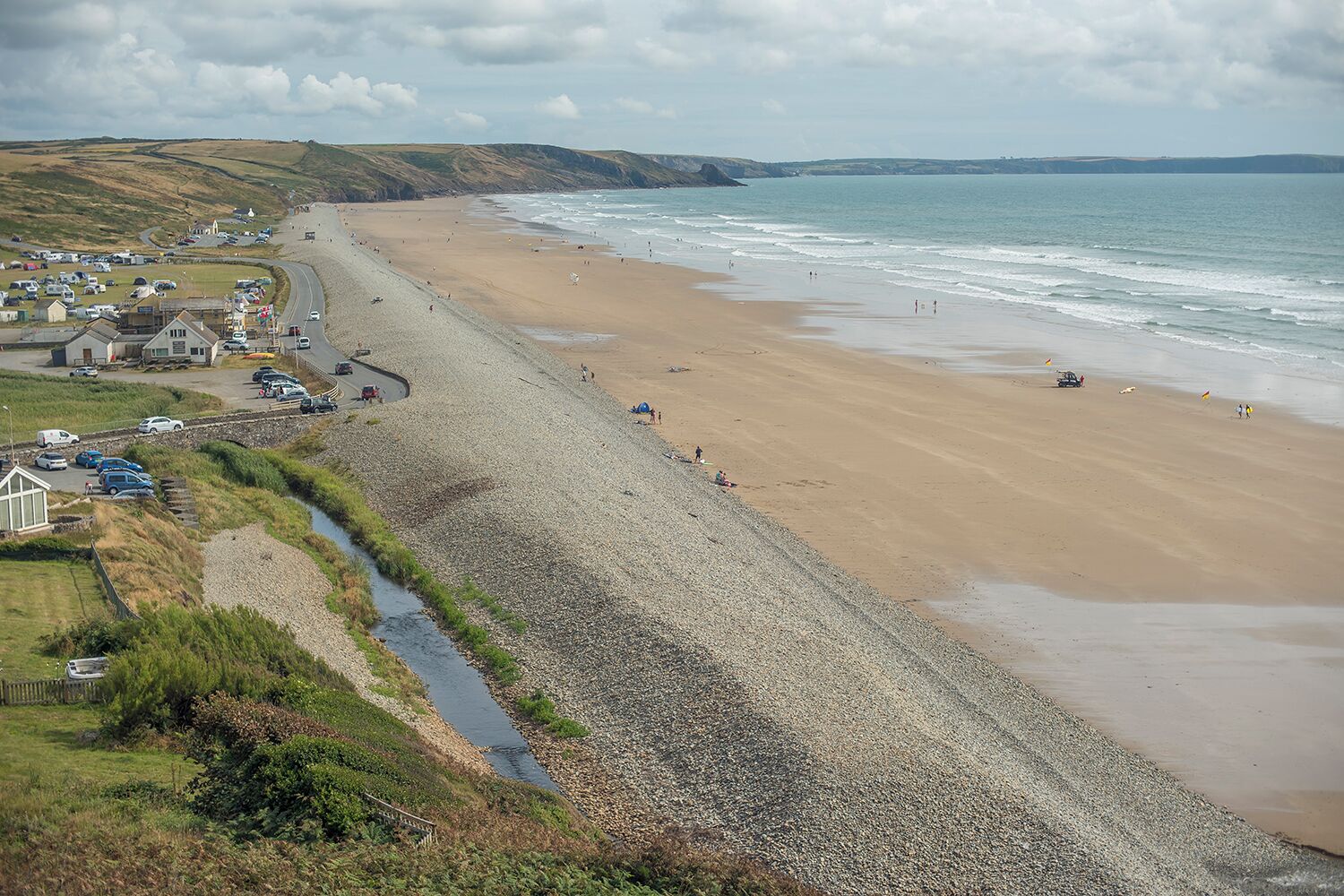 Une route côtière menant à une plage, avec un petit village et un ruisseau à proximité.