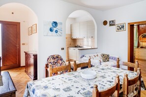 A dining area with a round table, chairs, and a bench. There is a kitchen with white cabinets and a sink. - Apartment 'Principina tra mare e natura' with Shared Pool, Wi-Fi and Air Conditioning (Principina Terra)