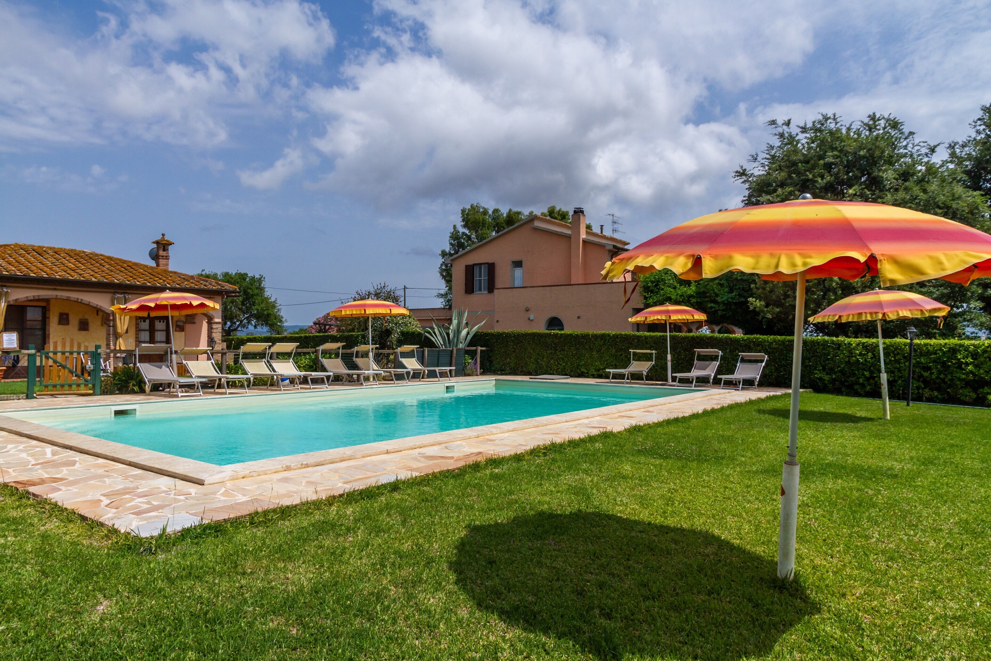 Une piscine entourée de chaises longues et de parasols, avec une pelouse bien entretenue et une maison en arrière-plan.