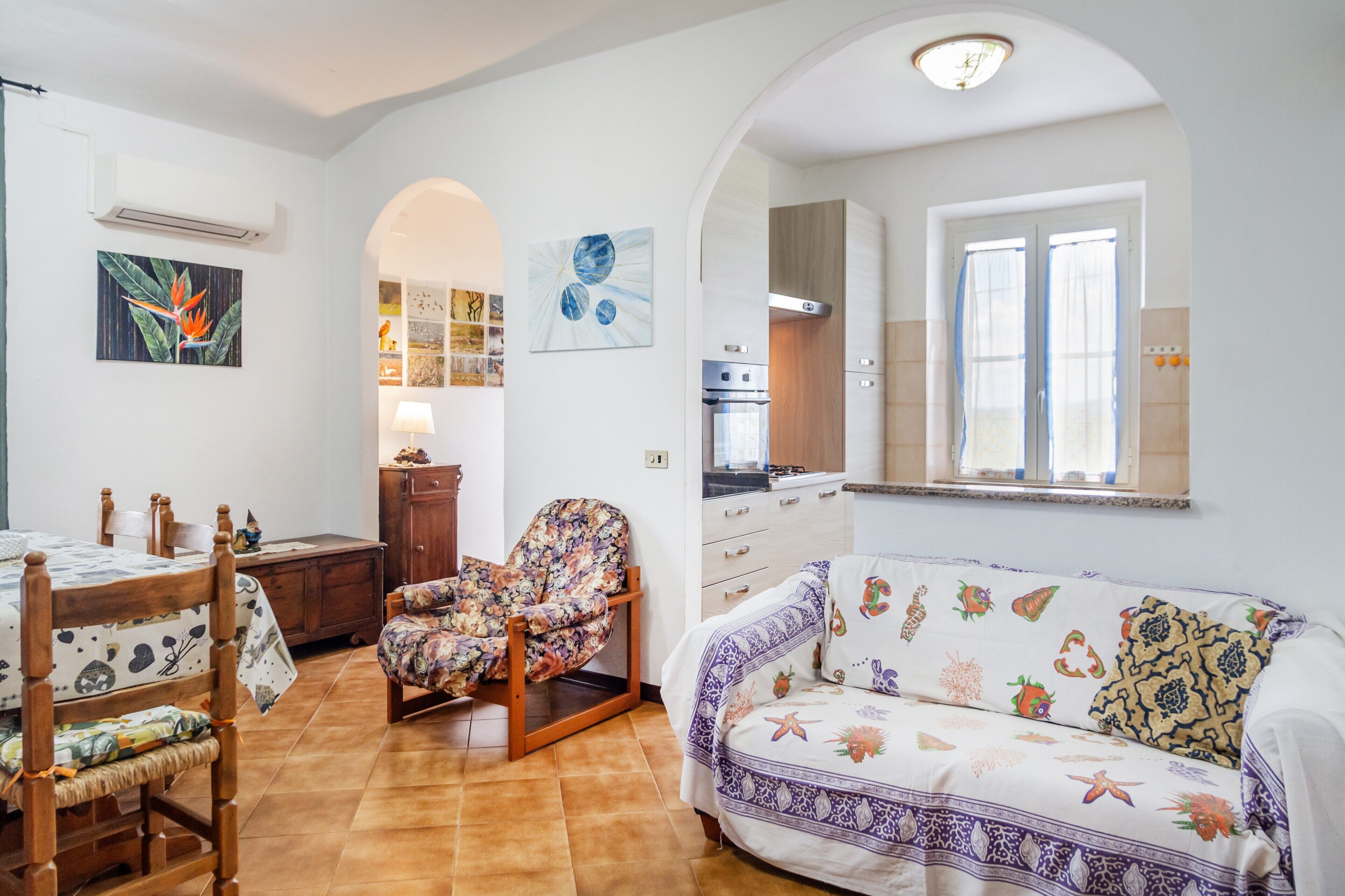 Una sala de estar con un sofá, una silla, una mesa de comedor y una zona de cocina visible a través de un arco.