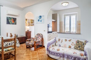 A living room with a sofa, a chair, a dining table, and a kitchen area visible through an archway. - Apartment 'Principina tra mare e natura' with Shared Pool, Wi-Fi and Air Conditioning (Principina Terra)