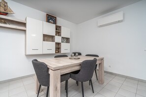 Ein Essbereich mit Holztisch, grauen Stühlen, weißen Schränken und einem Schiffsmodell im Regal.