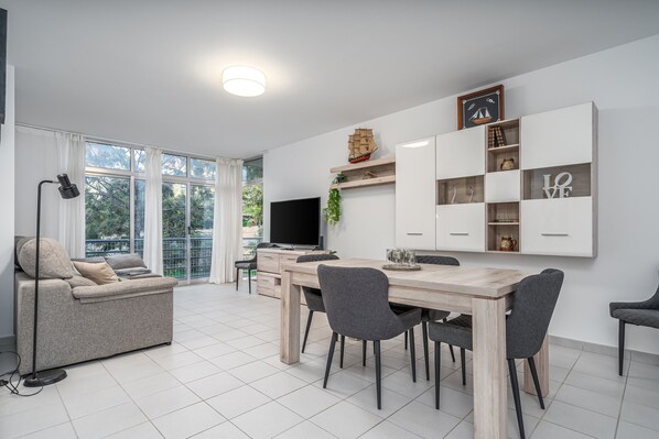 A modern living room with a sofa, dining table, chairs, a TV, and a bookshelf. - Apartment 'Sea Breeze' with Balcony, Wi-Fi and Air Conditioning (Portimão)