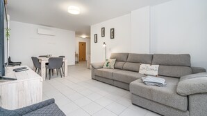 Una sala de estar moderna con sofá, una mesa de centro, televisor y un comedor con sillas y una mesa.