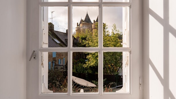 Una ventana con vistas a un castillo, un jardín y un edificio con contraventanas azules.