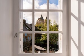 Una ventana con vistas a un castillo, un jardín y un edificio con contraventanas azules.