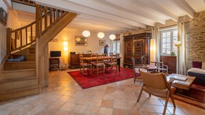 Amplia sala de estar con una escalera de madera, una mesa de comedor con sillas, un tapete rojo y una pared de piedra.