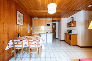 A wooden interior with a dining table, chairs, a kitchen area, and a small cabinet. - Apartment 'Bergeronnette' with Mountain View, Shared Terrace and Wi-Fi (La Giettaz)