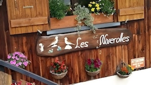 En træbygning med et skilt der siger 'Les Viveroles', et vindue med gardiner og blomsterkasser på gelænderet.
