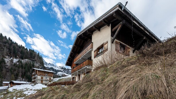 Ein mehrstöckiges Chalet mit Balkonen, gelegen an einem Hang mit Blick auf Berge.