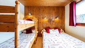 Ein Schlafraum mit Etagenbetten, Holzwänden und -decke, zwei Nachttischlampen und einem Fenster mit Vorhängen.