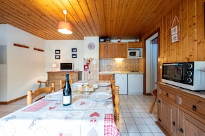 Une pièce aux murs lambrissés, avec une table à manger dressée pour deux personnes, un four à micro-ondes et un réfrigérateur.