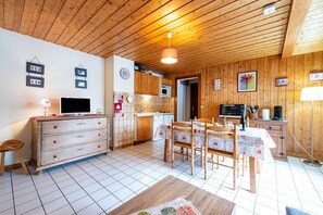 Une cuisine aux murs lambrissés, avec une table à manger et des chaises, un téléviseur et un four à micro-ondes.