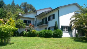 A two-story building with balconies, surrounded by greenery and trees. - Casa Pinho – Private Jacuzzi, Mountain View & Fireplace (São Pedro do Sul)