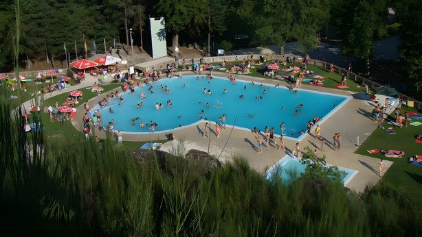 A large outdoor swimming pool surrounded by grass and trees, with several umbrellas and lounge chairs. - Casa Pinho – Private Jacuzzi, Mountain View & Fireplace (São Pedro do Sul)