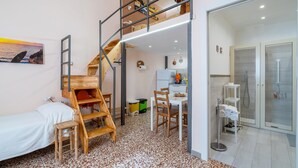 A compact room with a bed, a dining table, a staircase, and a shower area.