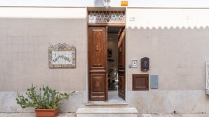 A building entrance with a wooden door, a potted plant, and a tiled wall.