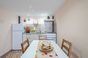 A compact kitchen with white appliances, a dining table with a floral tablecloth, and a brick backsplash.