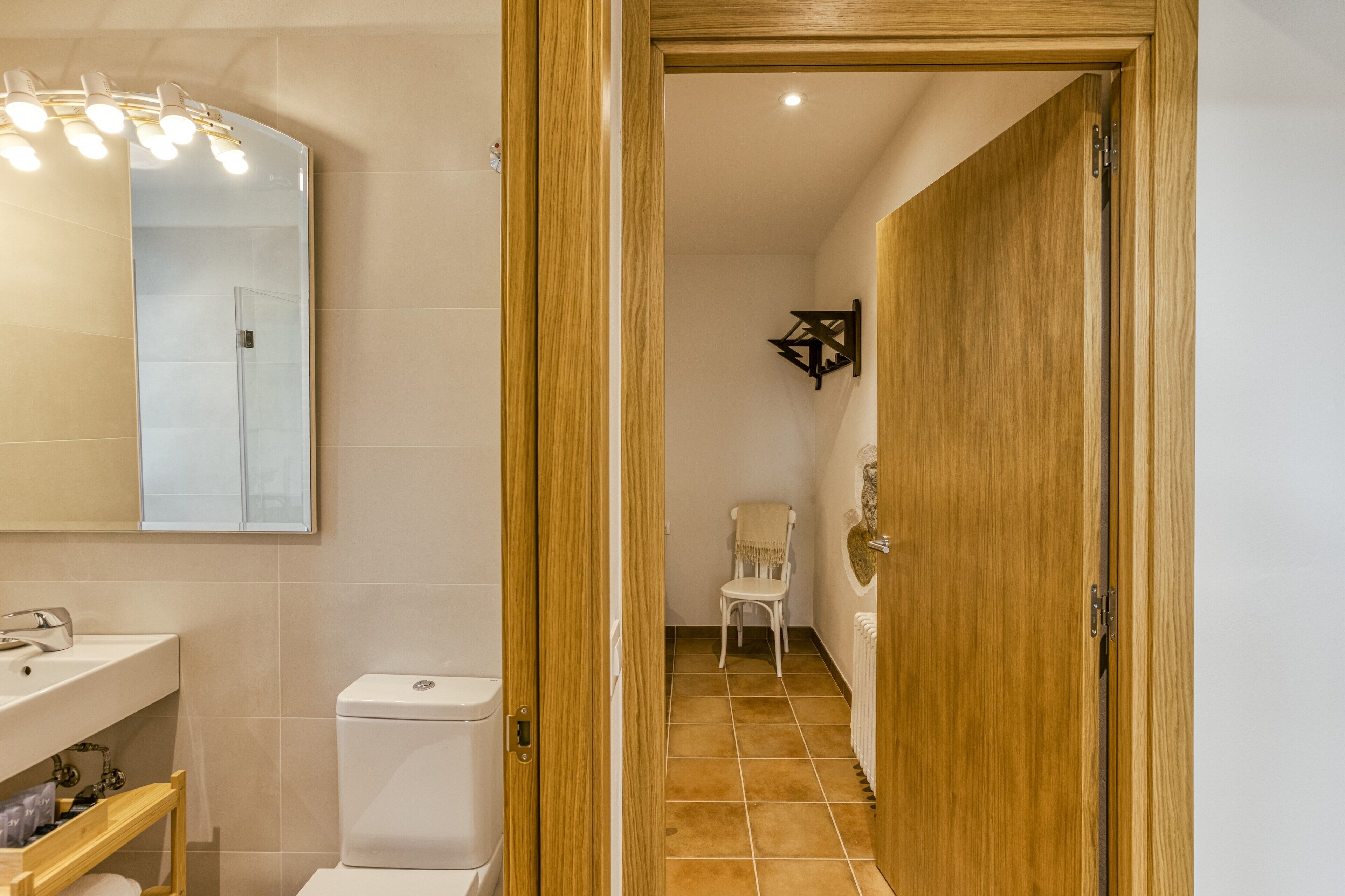 A bathroom with a toilet, sink, mirror, and a chair.