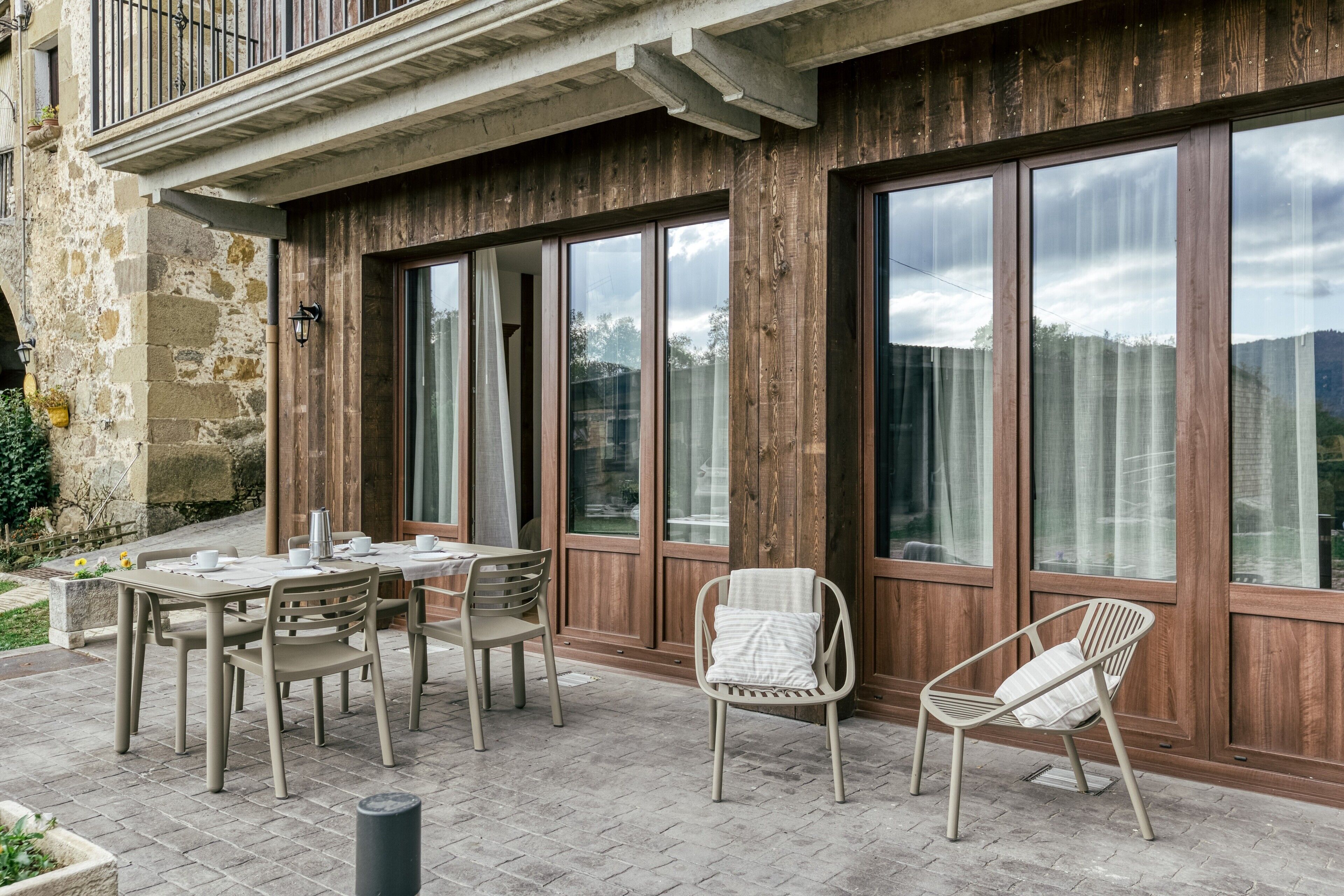 Une terrasse extérieure avec une table et des chaises, de grandes fenêtres et un mur en bois.