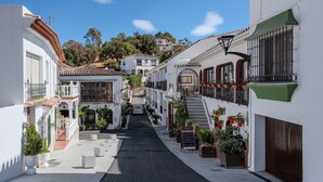 A narrow street with white buildings, a paved walkway, and potted plants. - Apartment '3 Bed  in Benahavis' with Mountain View, Wi-Fi and Air Conditioning (Benahavís)